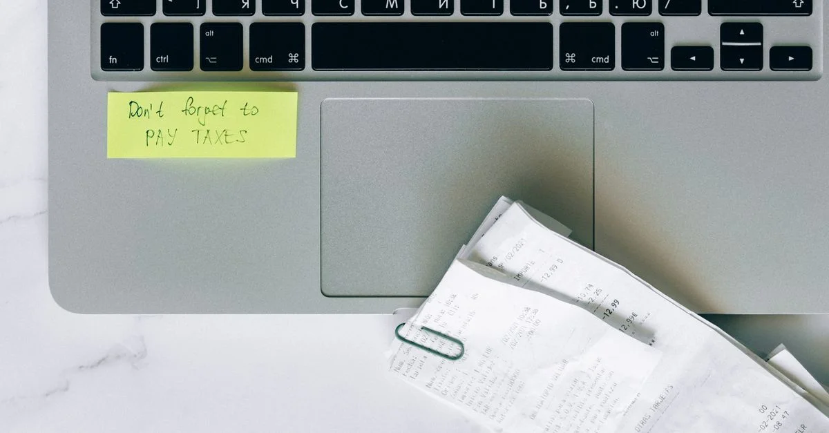 Un ordinateur portable avec un post-it de rappel et des reçus, soulignant l'organisation pour la saison des impôts.
