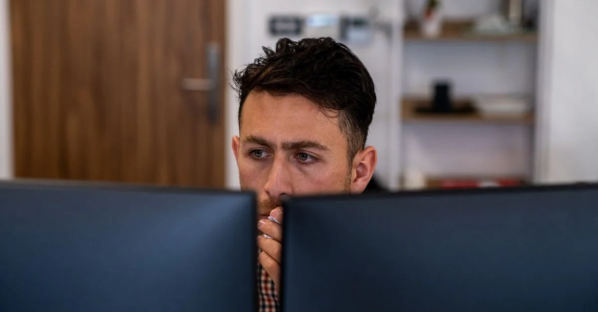 Homme profondément concentré sur son travail à son bureau avec des doubles écrans.