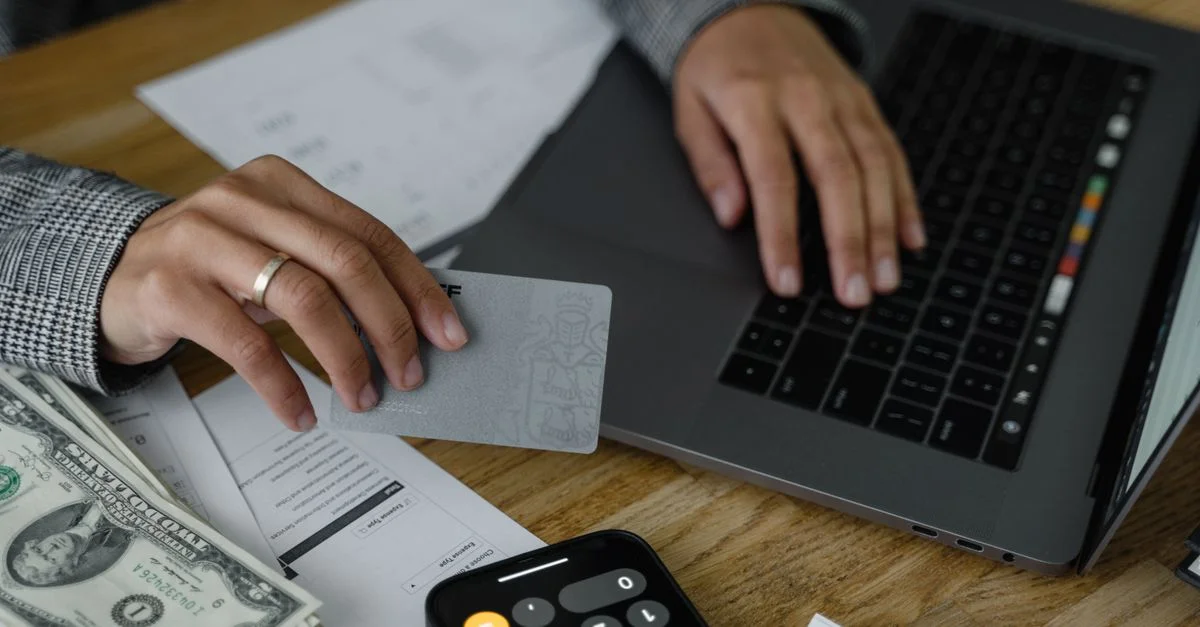 Gros plan d'une personne utilisant une carte de crédit et un ordinateur portable dans un cadre financier avec de l'argent et une calculatrice.