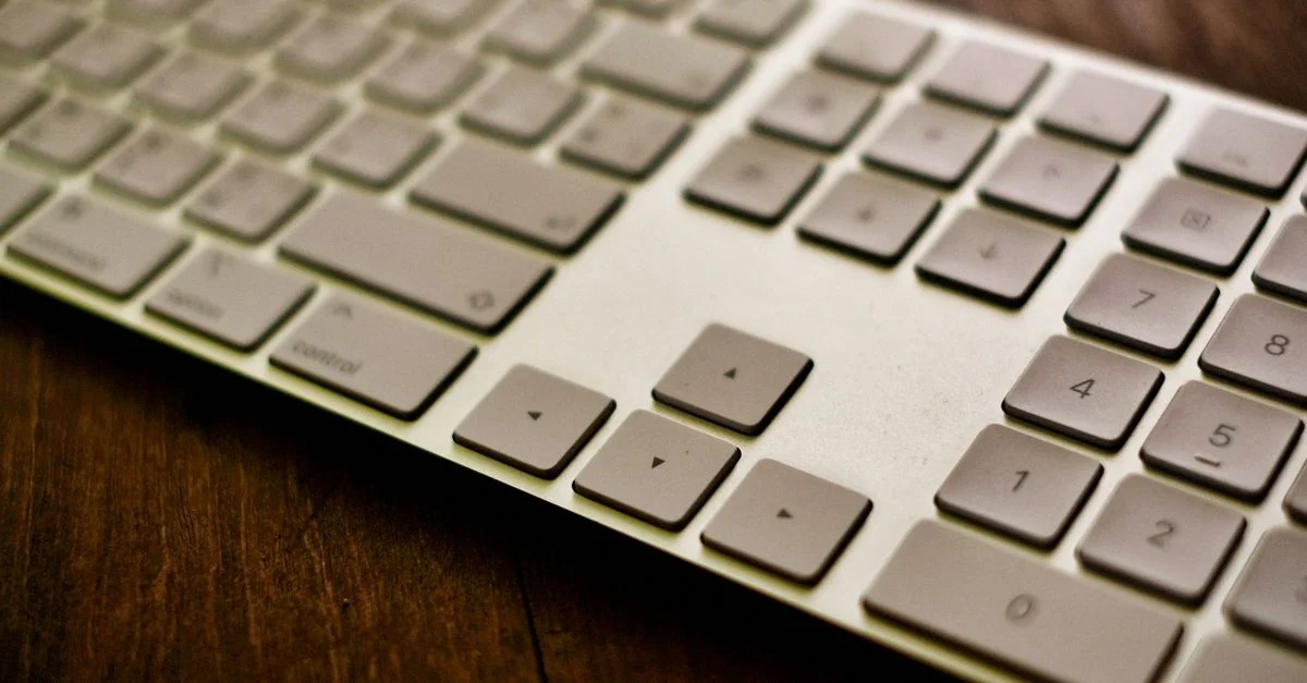 Gros plan stylisé d'un clavier blanc moderne placé sur un bureau en bois.