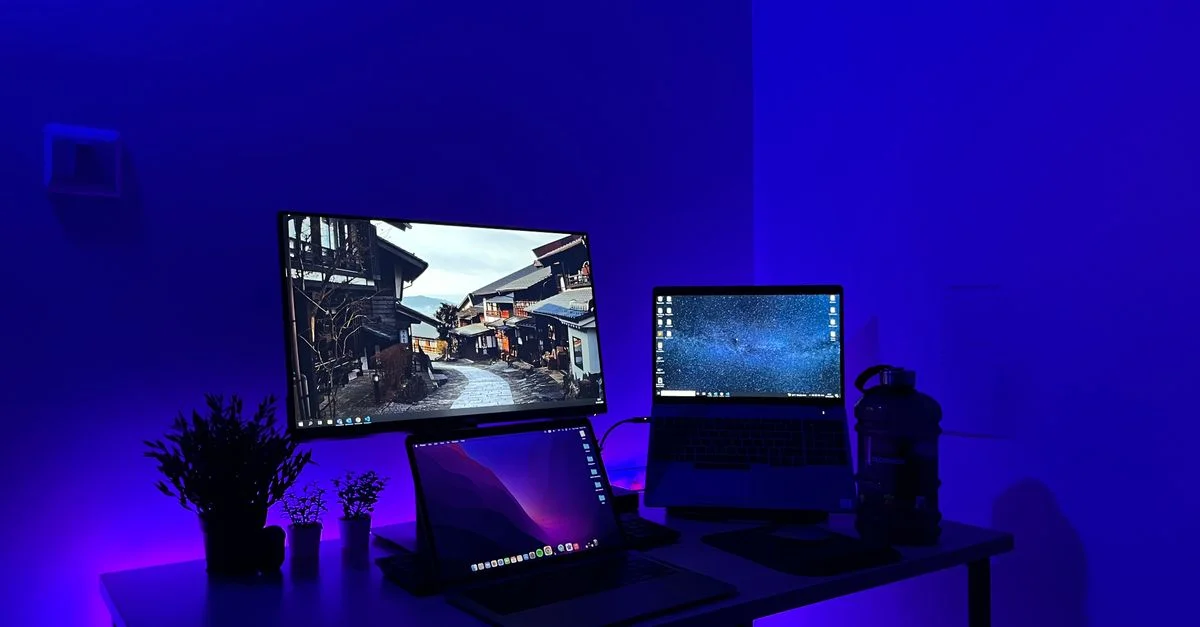 Configuration de bureau de jeu élégante avec plusieurs écrans et éclairage néon bleu, parfaite pour les passionnés de technologie.