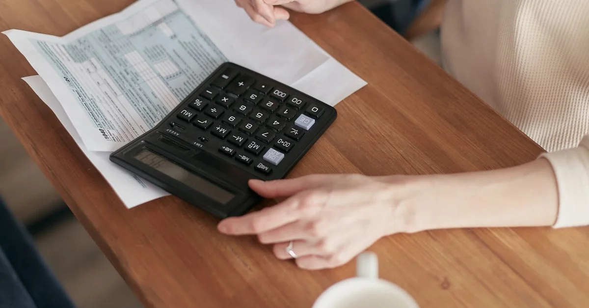 Individu concentré utilisant une calculatrice pour gérer ses finances personnelles à un bureau en bois.