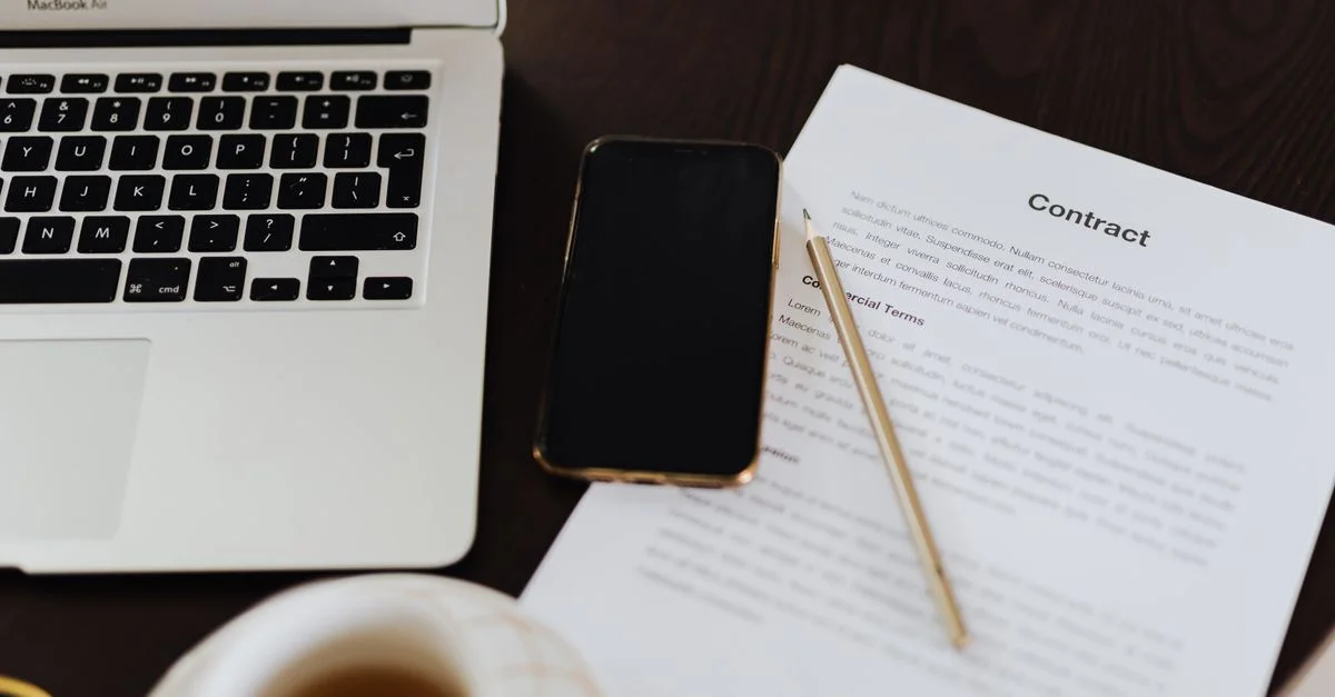 Gros plan d'un espace de travail avec un contrat, un ordinateur portable, un smartphone et une tasse de thé.