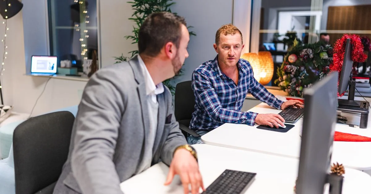 Deux hommes collaborent dans un bureau moderne avec des ordinateurs et une décoration festive.